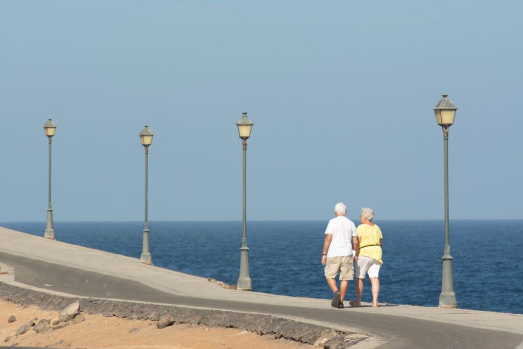 海沿いの遊歩道を歩くシニア夫婦の後ろ姿（健康・長生き）